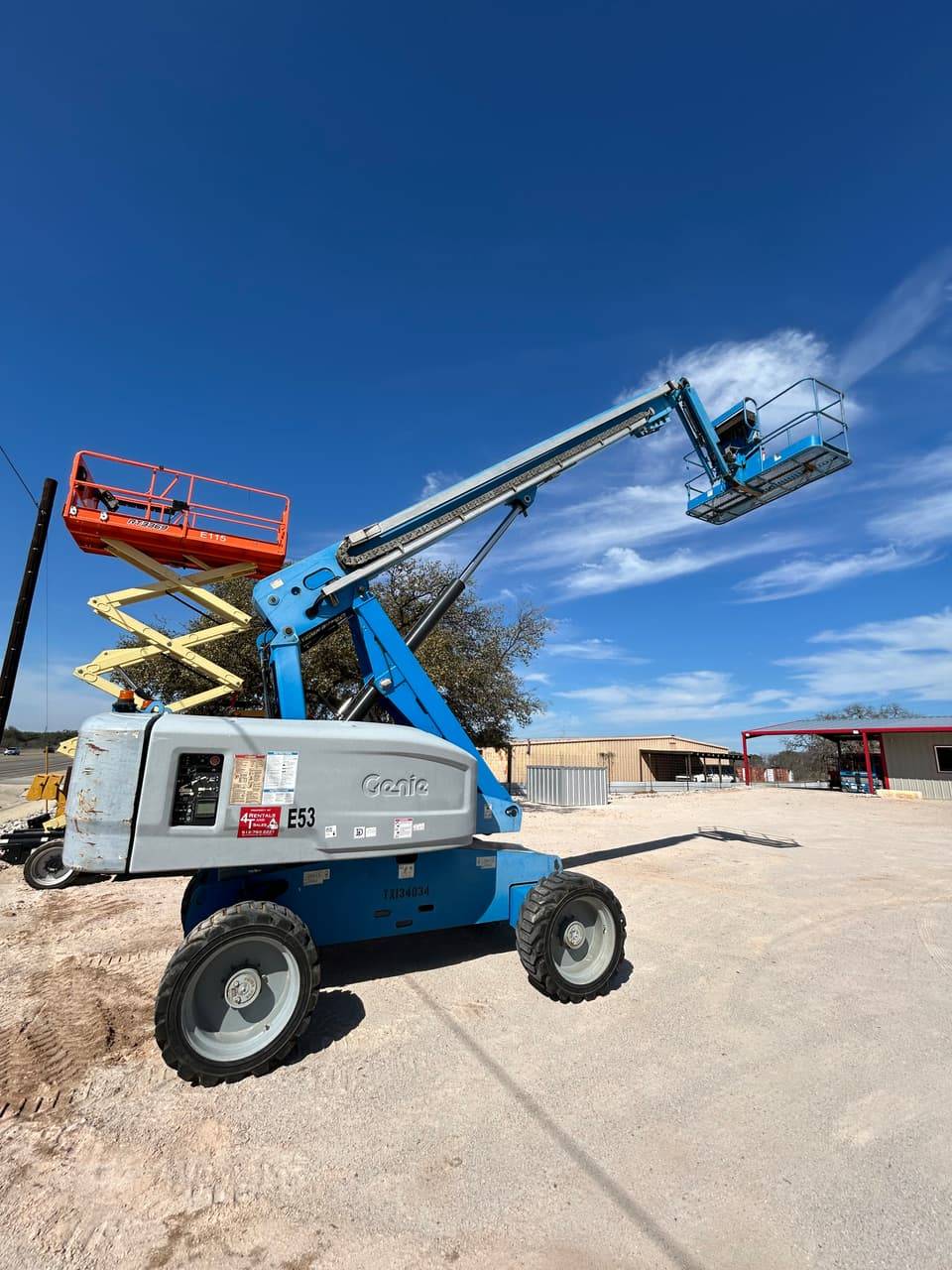 Genie articulating boom lift beside an orange JLG scissor lift on the 4-T Rental & Sales yard